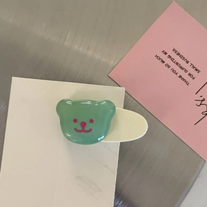 Niedliche grüne Bären-Haarklammer auf Marmorkarte mit rosa Dekoration Hintergrund