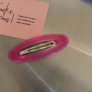 Close-up of pink translucent oval hair clip with visible metal mechanism on metal surface