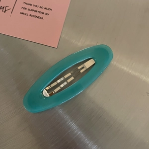 Close-up of cyan oval hair clip with smooth acrylic finish on metallic background