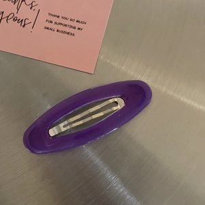 Detailed view of a purple oval snap clip on a metallic surface with a thank you card