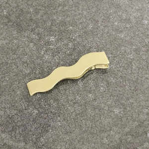 Barrette à cheveux ondulée en métal doré avec une finition mate brossée sur fond de pierre