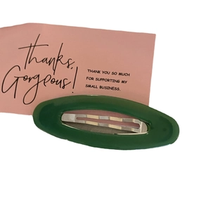 Glossy dark green oval hair clip with silver metal snap on pink card background