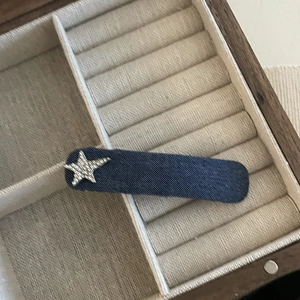 Detailed view of a navy denim oval hair clip with a sparkling rhinestone star on a tray