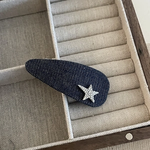 Close-up of a blue denim star hair clip with glitter details in a jewelry box