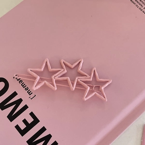 Pince à cheveux étoile rose mate avec trois étoiles évidées sur carnet couleur pastel