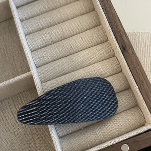 Close-up of a blue denim fabric teardrop hair clip resting in a wooden jewelry box