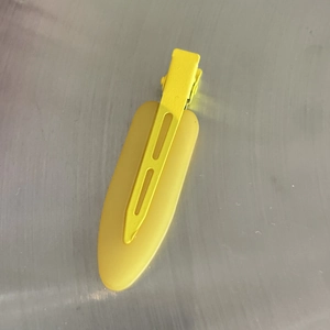 Detail view of the yellow matte non-marking duckbill hair clip on a metal surface