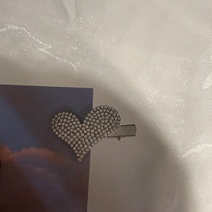 Detailed close-up of a heart-shaped silver metal hair clip with sparkling rhinestones