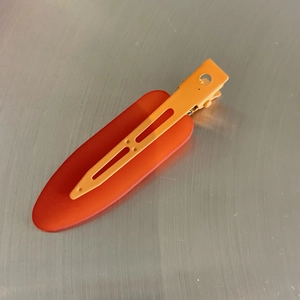 Detail view of a matte orange seamless hair clip with a spring duckbill mechanism