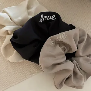 Close-up of three satin scrunchies in cream, black, and coffee with love embroidery