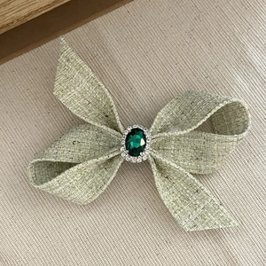 Fermaglio fiocco in tweed verde con pietra smeraldo e bordatura di strass luminosi