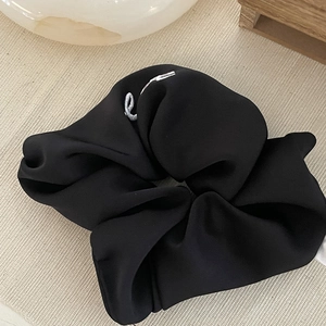 Detailed close-up of a black satin scrunchie with white 'e' embroidery on a textured surface