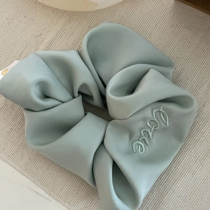 Close-up of mint green satin scrunchie featuring elegant Love embroidery detail
