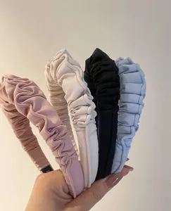 Detail of four pleated fabric headbands in pink, beige, black and blue held by hand