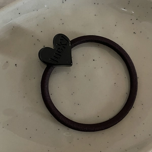 Dettaglio dell'elastico per capelli nero con ciondolo a cuore inciso lucky su vassoio ceramica