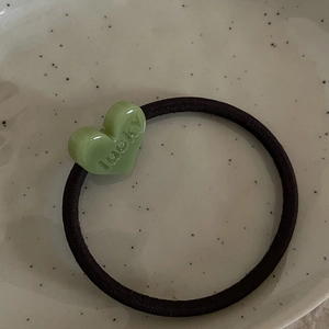 Dettaglio di un elastico per capelli con cuore in resina verde chiaro e incisione Lucky