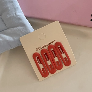 Close-up of four matte red oval BB hair clips displayed on a beige accessories card
