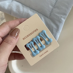 Detailed view of three sky blue bone-shaped hair clips on a handmade card display