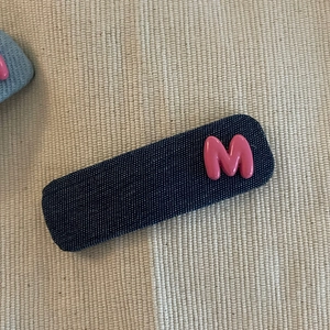 Gros plan sur la barrette en jean bleu avec un ornement lettre M rose en relief 3D