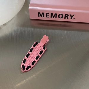 Barrette en métal rose avec détail de ruban noir posée sur un plateau argenté