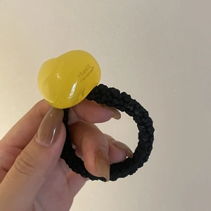 Detail view of a yellow translucent heart charm on a black braided elastic hair tie