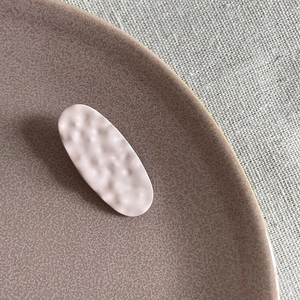 Pink oval hair clip with hammered texture on a ceramic plate with linen background