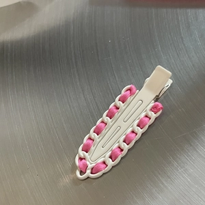 Détail d'un ruban en satin rose tissé dans une barrette à cheveux en chaîne blanche