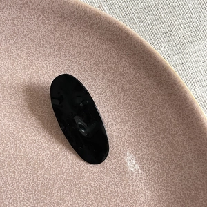 Macro shot of minimalist black glossy hair clip on a pink ceramic plate and linen background