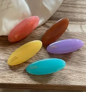 Flat lay of five candy-colored oval resin hair clips on soft wood and linen fabric