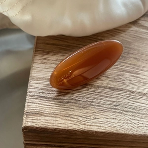Detailed macro view of an oval brown resin hair clip featuring a gold handmade logo