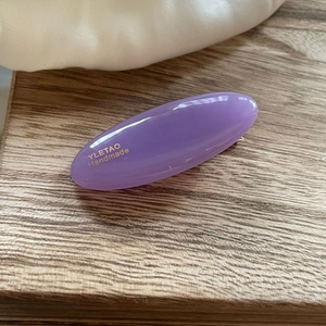 Macro view of a purple oval hair clip with gold handmade lettering on wood surface