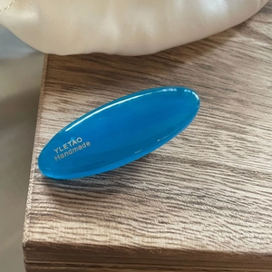 Minimalist oval candy-colored blue resin hair clip on a natural wooden background