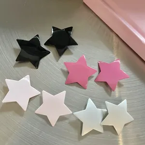 Close-up of four pairs of glossy star-shaped stud earrings in pink, white and black