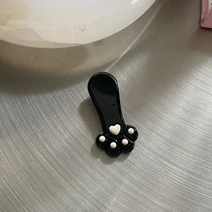 Detailaufnahme einer glänzenden schwarzen Katzenpfoten-Haarspange mit weißen Herz-Details