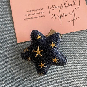 Détail macro de la pince à cheveux étoile en denim avec broderie dorée et clip bec de canard