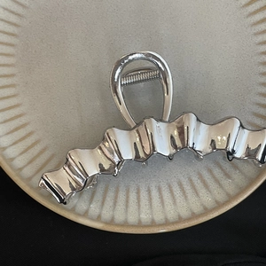 Polished silver metal wave hair claw clip for women on a textured beige dish