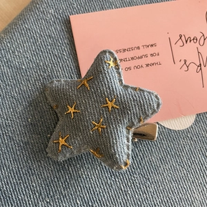 Détail d'une pince à cheveux étoile en denim gris avec broderie dorée et clip en métal