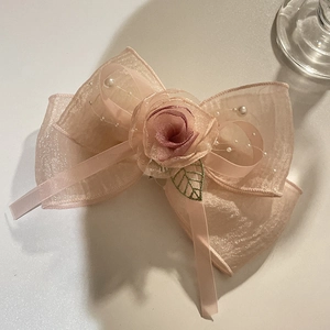Pink oversized organza bow hair clip with fabric rose and pearl details on white surface