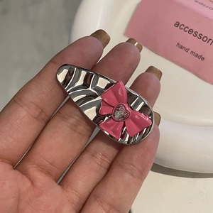 Barrette en métal argenté avec nœud rose et strass en cœur tenue sur plateau