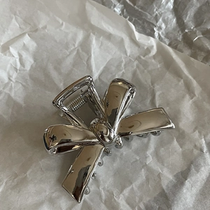 Minimalist silver metal bow hair claw clip for women on a white textured background