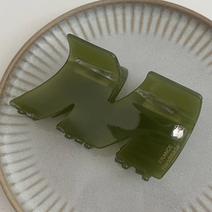 Dettaglio di un mollettone in acetato verde scuro con strass quadrato e scritte oro