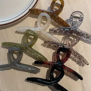 Diverses grandes pinces à cheveux en acrylique de 14 cm sur une surface beige texturée