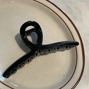 Vue de dessus d'une pince à cheveux de 14 cm en acrylique noir brillant sur une assiette