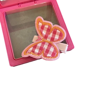 Cute pink checkered butterfly hair clip with embroidery detail on a makeup box background
