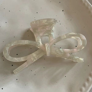 Top view of a pearlescent acetate bow hair claw clip on a ceramic display plate