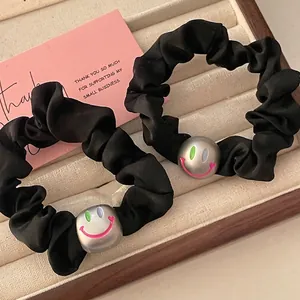 Black satin scrunchie with metallic smiley face beads on a beige jewelry display tray