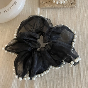 Gros plan sur un chouchou en maille noire orné d'élégantes perles blanches