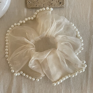 Détail d'un chouchou en organza beige avec perles blanches sur fond texturé élégant