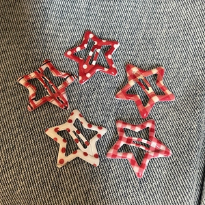 Close-up of five colorful Y2K star-shaped BB hair clips on a denim fabric background