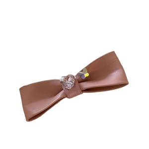 Barrette nœud en cuir rose avec cristal en cœur et détail papillon iridescent sur blanc